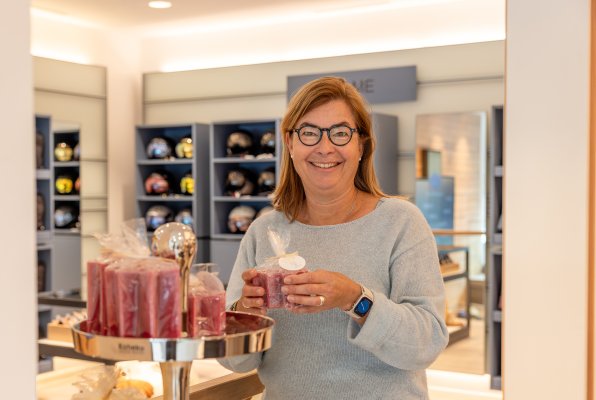 Lächelnde Mitarbeiterin, die eine verpackte Kerze in den Händen hält und direkt in die Kamera blickt