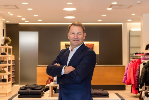 Geschäftsführer Wolfgang Gruber steht mit verschränkten Armen lächelnd in der Modeabteilung des Sportgeschäfts.